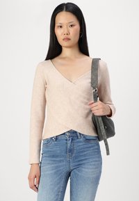 Hellrosa, langärmlige Wickeloberteil aus weichem Material mit tiefem V-Ausschnitt. Kombiniert mit blauen Jeans und einer grauen Umhängetasche.