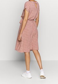 Robe florale rouge avec une coupe ample, des manches courtes et un détail en forme de trou de serrure dans le dos. Associée à des baskets blanches et des chaussettes jusqu'à la cheville.