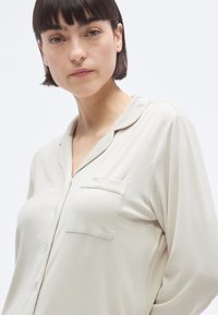 Ελαφριά μπεζ πουκάμισο με κουμπιά, απαλής ριμπ υφής, με μία τσέπη στο στήθος και γιακά. Μακριά μανίκια με άνετη εφαρμογή.