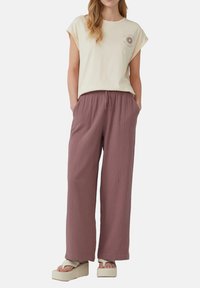 Crème katoenen t-shirt met korte opgerolde mouwen en zon grafiek, gecombineerd met losse roze gekreukte broeken en chunky beige plateau sandalen.