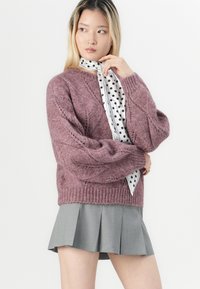 Pletena pulover u mekom, teksturiranom mauve tonu s kabel dizajnom i rebrastim manžetama, uparen s godinastom suknjom u sivoj boji i maramom s bijelim točkicama.