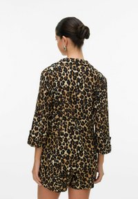 Set loungewear v leopardím vzoru v světle hnědé a černé barvě obsahující košili s límečkem a ohrnutými rukávy a odpovídající šortky, hladká textura.