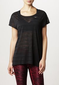 Camiseta atlética negra de manga corta, con una textura rayada y un pequeño logo de Nike en la parte delantera. Combinada con leggings rojos con estampado.