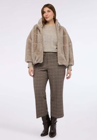 Beżowa kurtka z futerka ekologicznego z kapturem, sweter o fakturze oraz szerokie brązowe spodnie w kratę. Całość dopełniają czarne botki za kostkę.