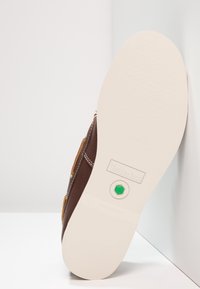 Braune Ledersohle mit weißem Boden, Timberland-Logo und einem kleinen grünen sechseckigen Emblem in der Mitte.