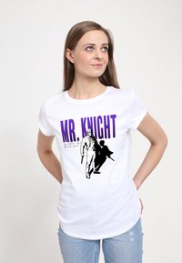 Bílý přiléhavý tričko s nápisem "MR. KNIGHT" v purpurové barvě. Čern�á grafika dvou postav, jedna drží zbraň, detailně vykreslená s obrysy a stíny.