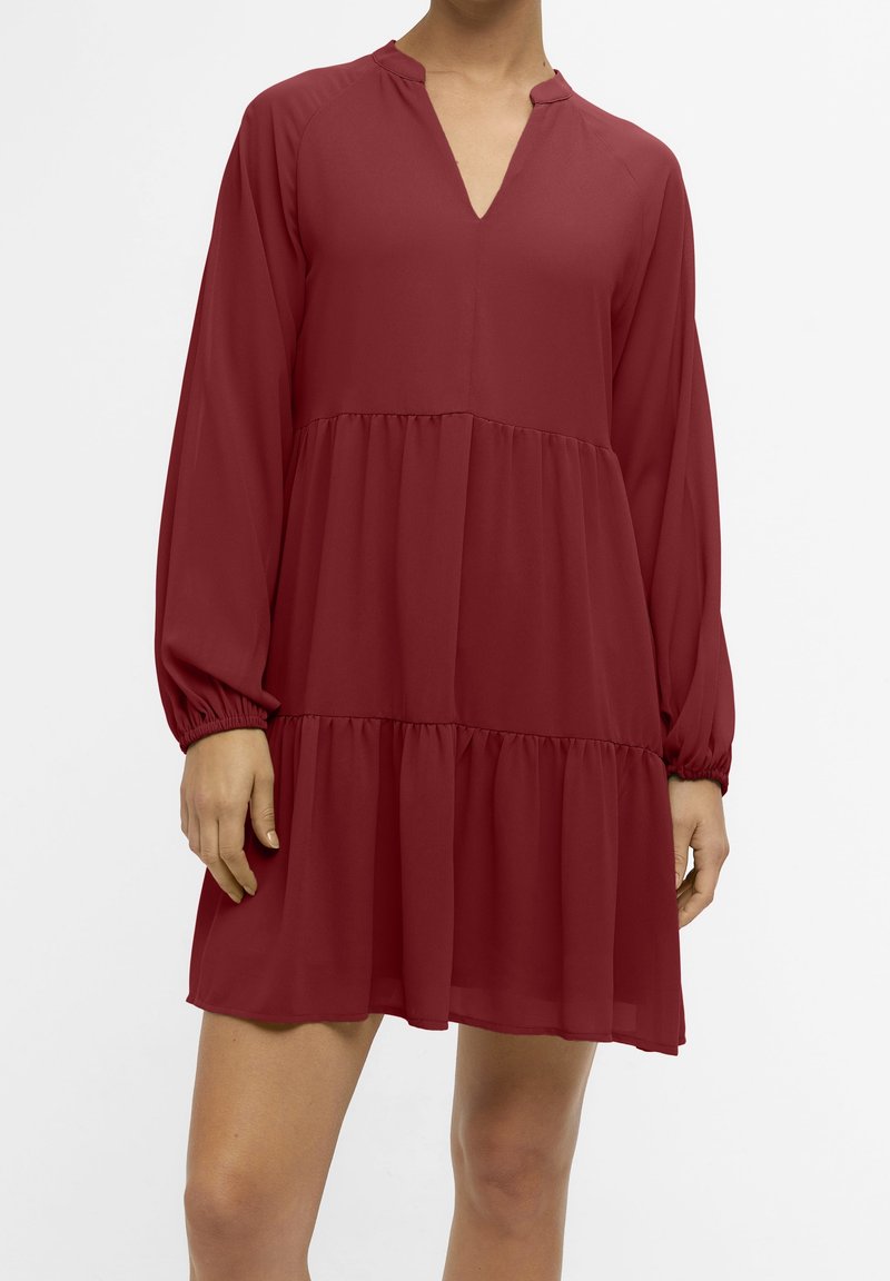 Robe longue à manches longues couleur bordeaux en tissu léger, présentant un col en V, des manches froncées et un design en volants avec un ourlet fluide.