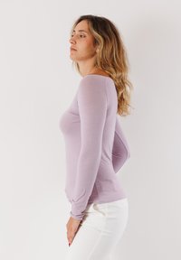 Top lungo viola chiaro con un design aderente, texture liscia e scollatura ampia, abbinato a pantaloni bianchi.