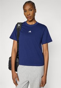 Tengerészkék pamut rövid ujjú póló kerek nyakkal és fehér logó díszítéssel. Szürke melegítőnadrággal és fekete táskával párosítva.