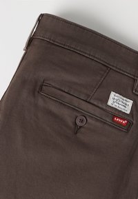Καφέ τσέπη παντελονιού Levi's με κούμπωμα κουμπιού, κόκκινη ετικέτα Levi's και λευκή ετικέτα μάρκας ραμμένη πάνω από την τσέπη.
