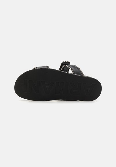 Black sandal with a textured rubber sole, featuring adjustable straps with braided accents. Base displays "ARMANI" in bold lettering.