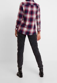 Plaid shirt in navy, burgundy, and cream tones with long sleeves and buttoned cuffs, paired with dark gray textured pants and black ankle boots.