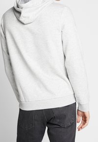 Grå huvtröja med texturerad tyg. Har ribbade manschetter och fåll, visas från baksidan, i kombination med mörka jeans.