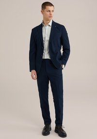 Costum de marin cu textură cu dungi fine, sacou cu un singur nasture și pantaloni croiți. Purtați cu o cămașă de culoare deschisă și pantofi eleganți negri.