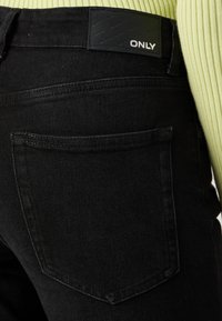 Blugi negri cu un material texturat, cusături vizibile și un design distinct al buzunarului din spate. Talie are un eticheta de marcă inscripționată "ONLY."