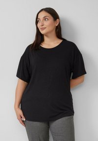 Czarny krótki top z krótkim rękawem, okrągłym dekoltem i miękką teksturą, z subtelnymi zdobieniami. W zestawie ze szarymi spodniami.