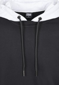 Fekete kapucnis pulóver fehér szegélyezett kapucnival, fém fűzővel ellátott zsinórokkal, bordázott mandzsettákkal és "URBAN CLASSICS" feliratú címkével.