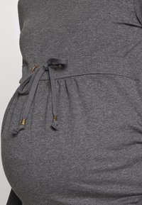 Šedý těhotenský top z měkké, elastické látky. Má nařasený pas se stahovací šňůrkou a zlaté doplňky pro nastavitelný střih.