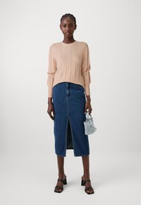 Pull en tricot rose clair avec un motif texturé et des manches longues, associé à une jupe midi en denim bleu avec une fente sur le devant et des sandales à talons bloc noires.