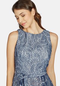 Navyblaue Spitze Kleid mit hochgeschlossenem Ausschnitt, ärmellosem Design, aufwendigen Blumenmustern und einer taillierten Taille mit Bindeband.