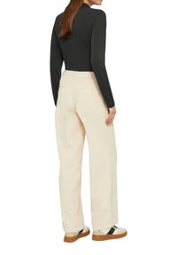 Cremfarbene, weit geschnittene Hose mit hohem Bund, Gesäßtaschen und glatter Textur, kombiniert mit einem enganliegenden schwarzen Langarmoberteil und flachen Schuhen.