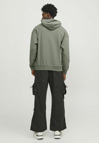 Felpa verde con un ampio cappuccio, vestibilità rilassata e polsini a costina. Abbinata a pantaloni cargo neri larghi con diverse tasche.