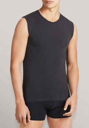 Uomo che indossa una maglietta nera aderente senza maniche e boxer neri abbinati, su uno sfondo semplice.