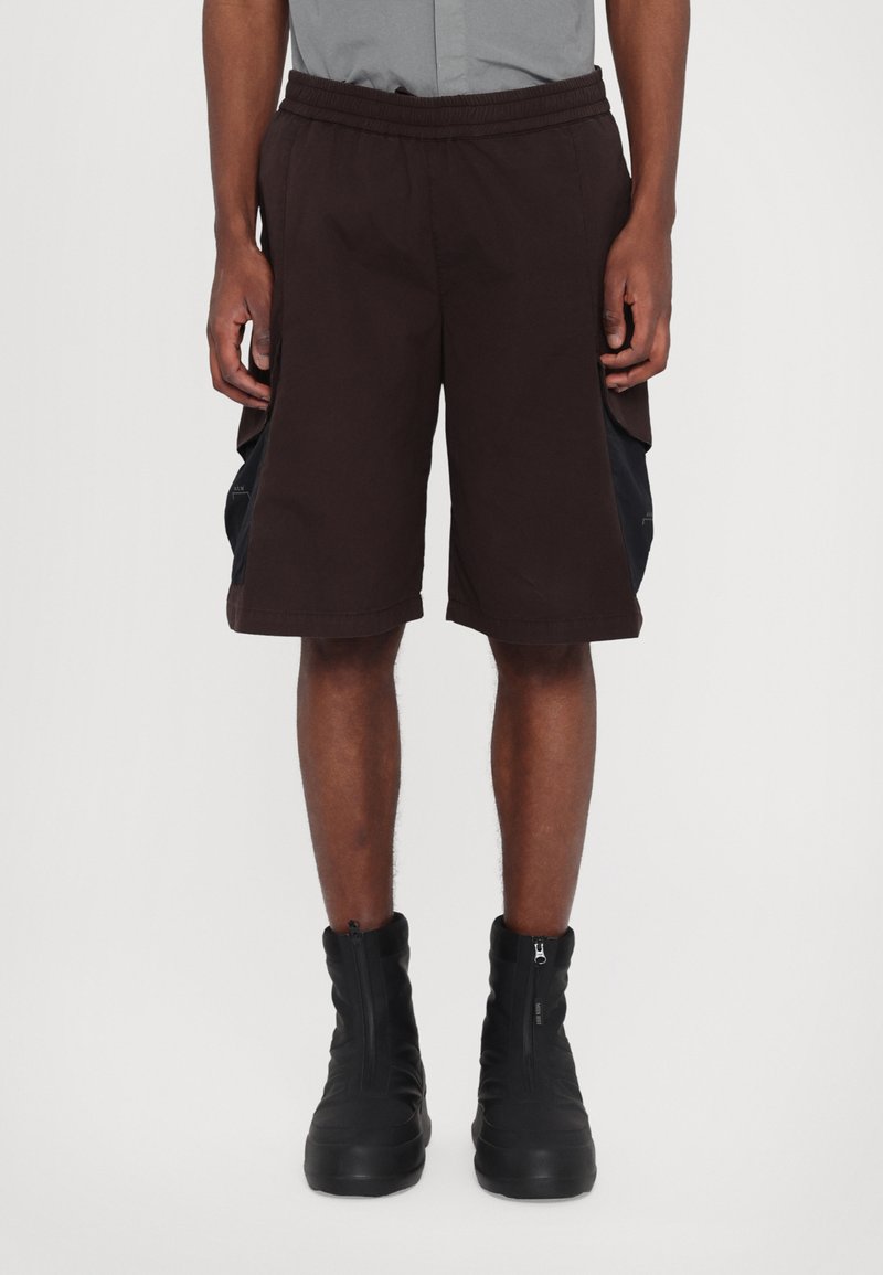 Shorts marron avec une taille élastique et des poches latérales, dotés d'accents noirs contrastants. Associés à des bottes noires zippées.