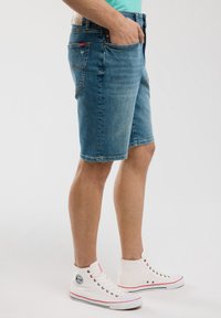 Gaiši zilie denimi šorti ar klasisku griezumu, ar priekšējām un aizmugurējām kabatām. Apvienoti ar baltām augstām kedām.