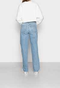 Ljust blå högmidjade jeans med rak passform, fem fickor och synlig sömnad; matchade med en vit oversized sweatshirt.