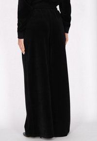 Czarne szerokie spodnie z welwetu o gładkiej fakturze i elastycznym pasku w talii; mają luźny krój oraz pełną długość.