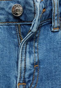 Ljusblå denimjeans har en metallknappstängning, dragkedja och orange sömmar längs sömmarna. Tyget visar subtil blekning.