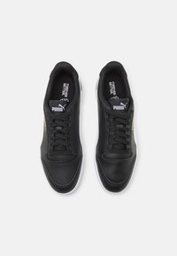 Baskets en cuir noir à texture lisse, bout arrondi, design à six œillets avec lacets, semelles extérieures en caoutchouc blanc, et détails de marque subtils.