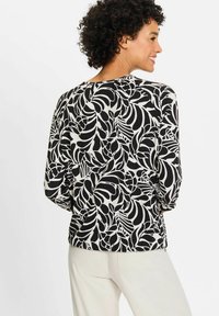 Langärmliges Oberteil in Schwarz und Creme mit einem Blättermuster, rundem Ausschnitt und lockerer Passform, von hinten gezeigt.