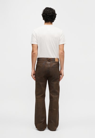 Καφέ δερμάτινο παντελόνι με ίσια γραμμή και εμφανείς λεπτομέρειες ραφής. Πίσω τσέπες και ζώνη με κόμπο. Άσπρο μπλουζάκι ορατό από πάνω.