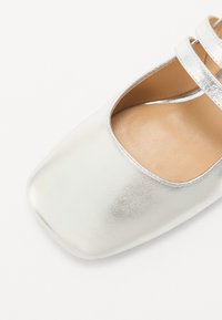 Ballerina argentata con punta quadrata, superficie metallica liscia e due cinturini decorativi. Fodera interna morbida in tan.