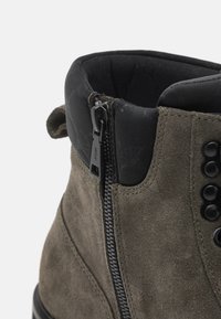 Bottines en daim vert olive avec des accents noirs, dotées d'une fermeture éclair latérale, d'un col rembourré noir et d'un design de bout arrondi.