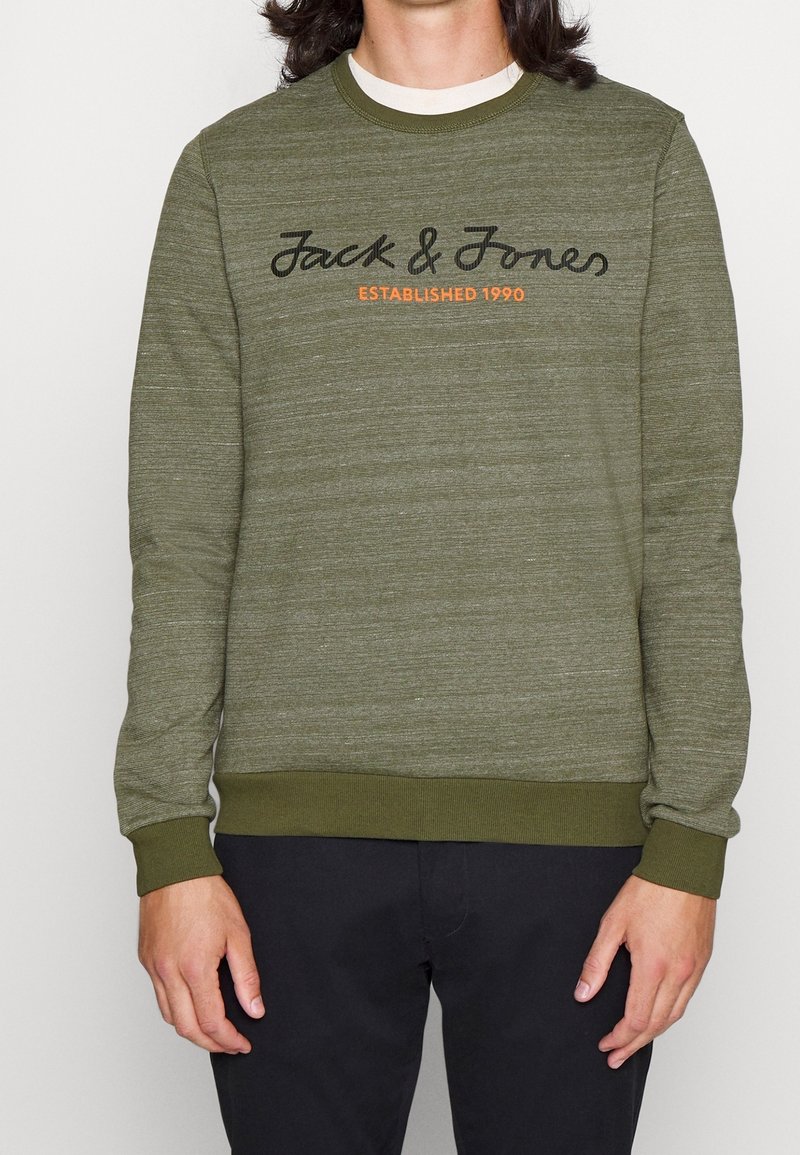 Felpa verde oliva realizzata in tessuto testurizzato, con un logo nero in script e il dettaglio dell'anno di fondazione arancione sul davanti. Polsini e orlo a costine.