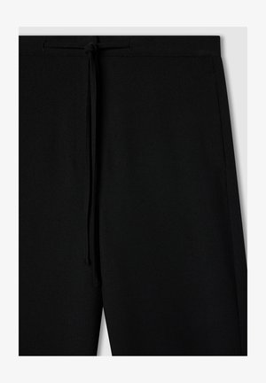 Pantaloni jogger neri con vita elasticizzata e cordoncino, texture liscia e cuciture laterali. Presentano una vestibilità rilassata e nessuna tasca visibile.