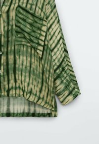 Camicia tie-dye verde e bianco sporco con vestibilità ampia, maniche lunghe, apertura con bottoni e taschino sul lato sinistro.