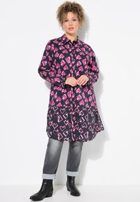 Schwarz-weißes Langarmhemdkleid mit pinkem abstraktem Muster, Knopfleiste vorne und Seitentaschen, kombiniert mit hochgekrempelten grauen Jeans und schwarzen Knöchelstiefeln.