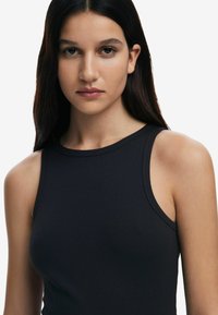 Top de tirantes negro con canalé, con escote redondo, diseño sin mangas y textura suave. Presenta un ajuste ceñido y sin patrones o acentos visibles.