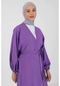 Purple, lightweight wrap dress with long, puff sleeves and a tied belt. The textured fabric drapes loosely. Topped with a grey hijab.