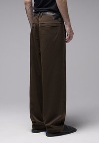 Pantalon large marron en tissu lisse, doté d'une taille haute, de poches arrière et d'une ceinture en cuir. Design soigné avec des détails minimaux.