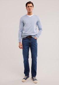 Suéter azul claro de pico sobre una camisa blanca, combinado con jeans azul oscuro y zapatillas azules. Atuendo informal con una silueta ajustada.