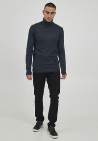 Sötétszürke, magas nyakú, hosszú ujjú póló, finoman textúrált anyagból, fekete slim fit nadrággal és fekete sportcipővel viselve.