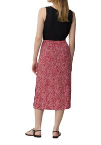Maxi skirt in red with a geometric white pattern. Soft fabric, loose fit, and side slits for ease of movement. Paired with a black tank top.