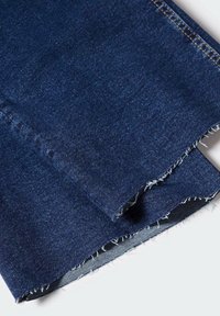 Tissu en jean bleu foncé avec des bords bruts et effilochés, plié sur une surface blanche.
