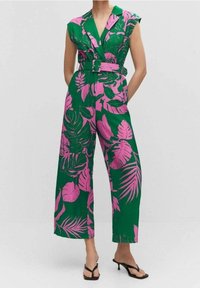 Combinaison verte avec motif de feuilles tropicales roses, manches courtes, taille ceinturée, pantalons larges, confectionnée dans un tissu léger.