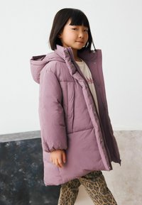 Lila Daunenjacke mit Kapuze, ausgestattet mit einem Reißverschluss und Druckknopfverschluss, gestepptem Design und Seitentaschen, getragen über einer Leggings im Leopardenprint.